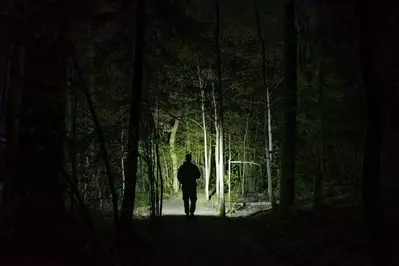 man holding a flashlight in the dark woods