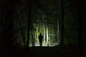 man holding a flashlight in the dark woods